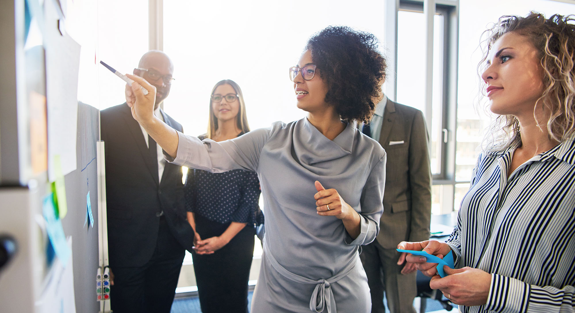 Diverse group of focused businesspeople brainstorming together on a whiteboard during a strategy session in a bright modern office