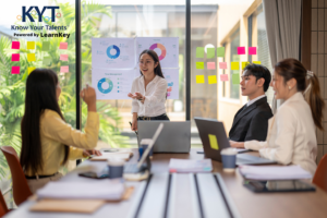 Facilitator leads a small team review of people-data charts and sticky-note plans, with the KYT Powered by LearnKey logo on the glass wall.