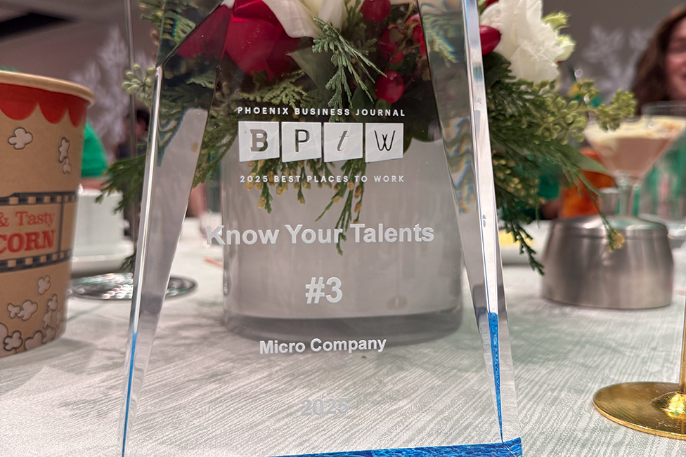 Clear geometric acrylic trophy in front of a flower centerpiece. The trophy reads "Phoenix Business Journal 2025 Best Places to Work: Know Your Talents #3 Micro Company 2025"