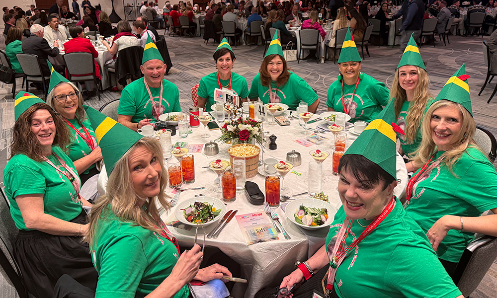 Ten Know Your Talents team members in green shirts and pointed hats—outfits inspired by the motion picture Elf—sit smiling at a round table at the annual Phoenix Business Journal Best Places to Work awards banquet