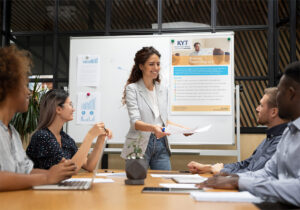 Facilitator leading a Team Impact workshop with a small group in a conference room using a whiteboard.