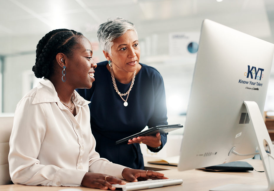 Experienced professional coaching a younger colleague at a computer, illustrating that AI-assisted work still depends on human expertise and judgment